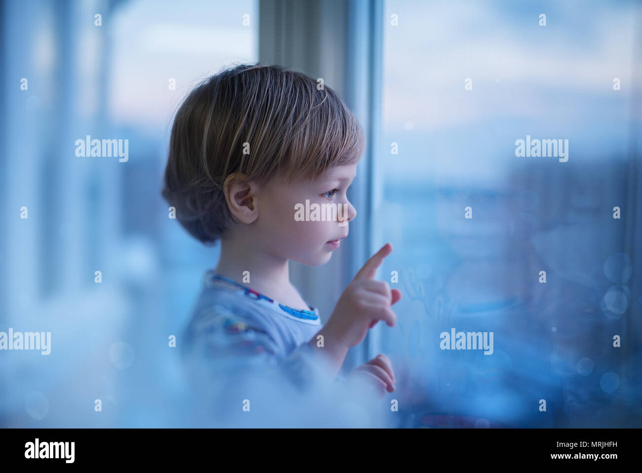 Cute zwei Jahr kind Blick auf Fenster in die Stadt. Weiche blaue romantische Tönung. Stockfoto