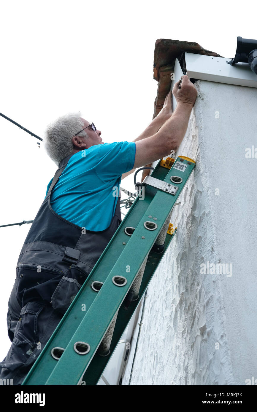 Ein Builder arbeiten auf einer Leiter die Regenrinne eines Hauses zu reparieren. Stockfoto