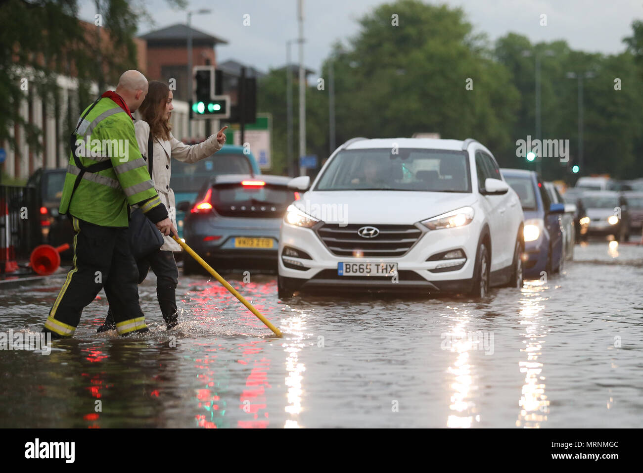 Feuerwehrmann hilft einer Frau Kreuz eine überflutete Straße, Birmingham, Großbritannien Stockfoto