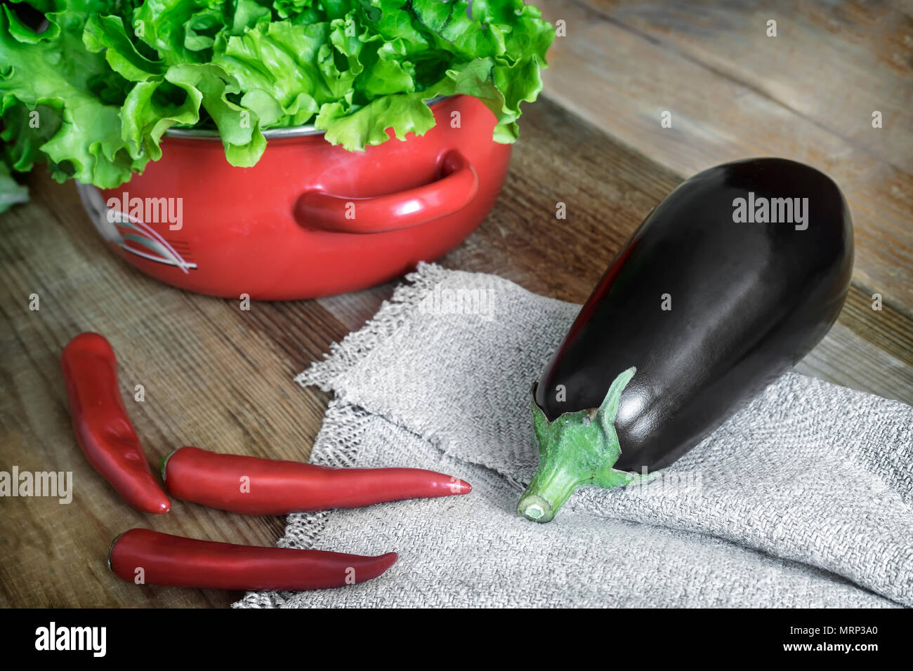 Auf einer hölzernen Tisch sind Gemüse: Auberginen, Chili und grünem Salat in einer kleinen roten Behälter. Stockfoto
