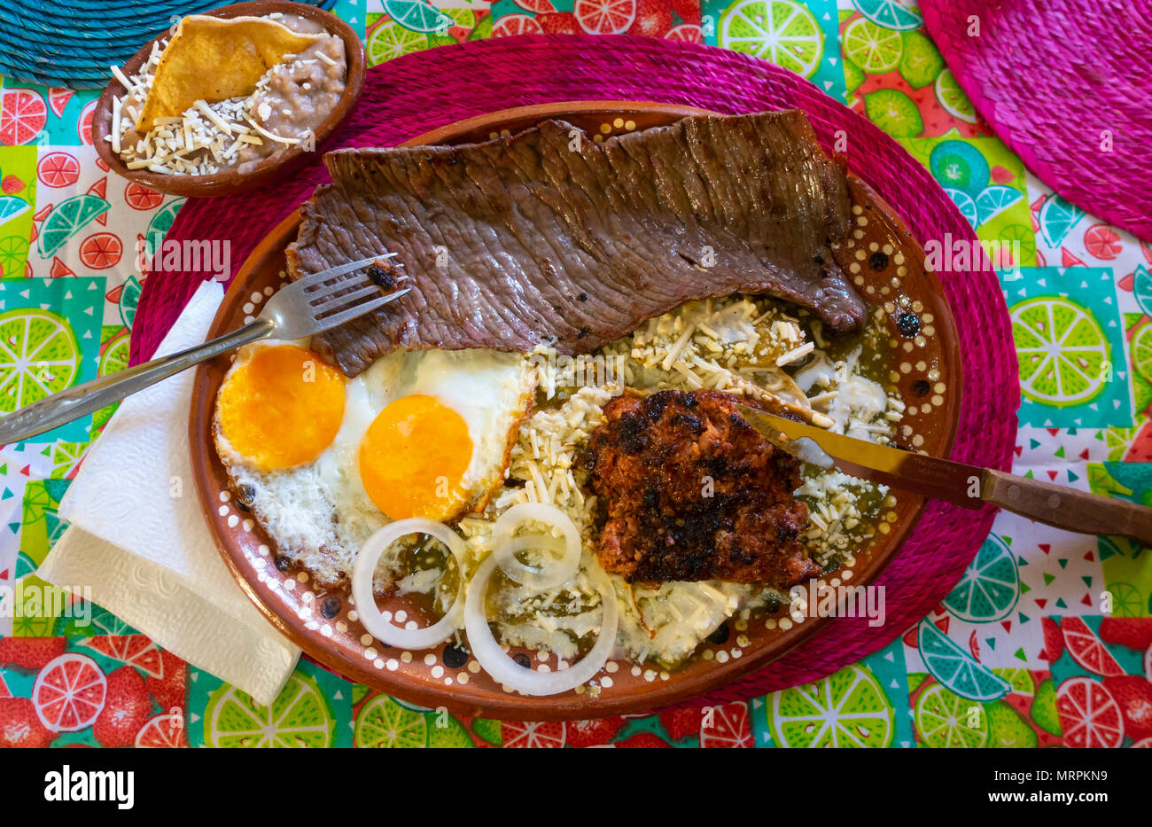 Ein komplettes mexikanisches Frühstück mit Steak, Wurst, Eiern, Bohnen, Käse, Tortillas und eine grüne Sauce. Stockfoto