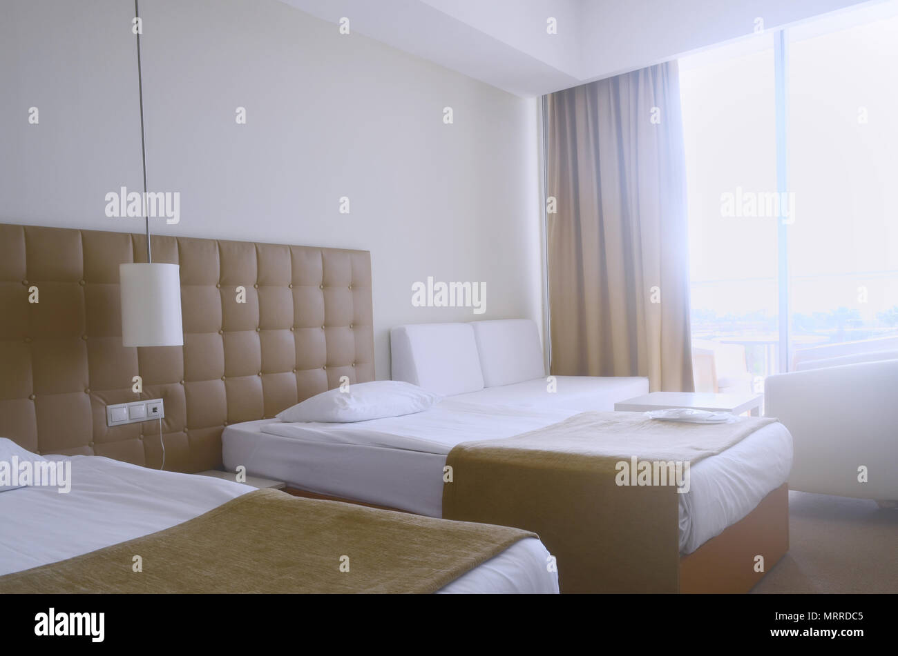 Sonnige Zimmer im Hotel in hellen Farben und mit zwei Betten, ein Sofa und eine Lampe Stockfoto