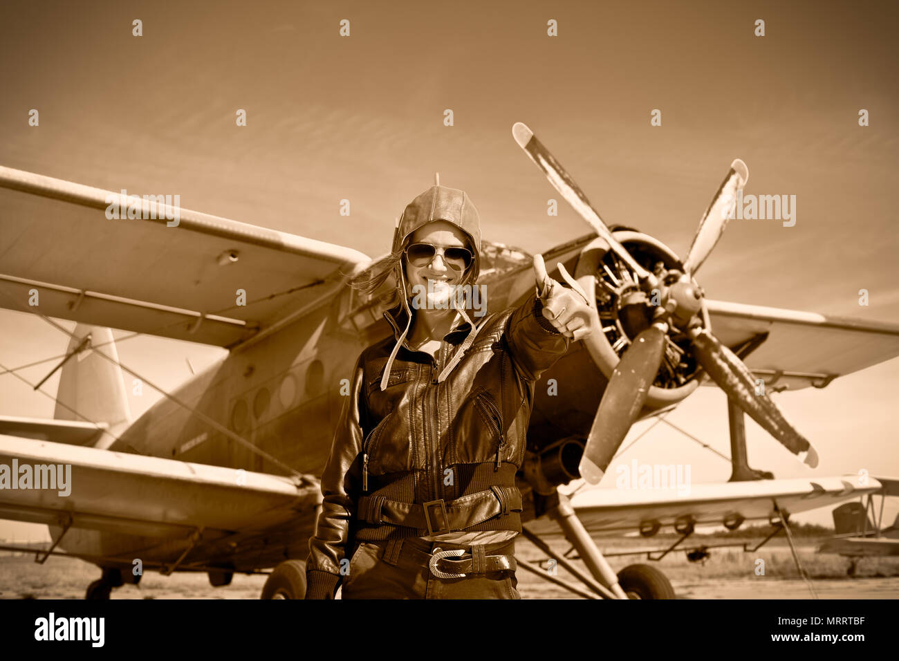 Portrait von schönen weiblichen Piloten mit dem Flugzeug hinter sich. Sepia Foto. Stockfoto