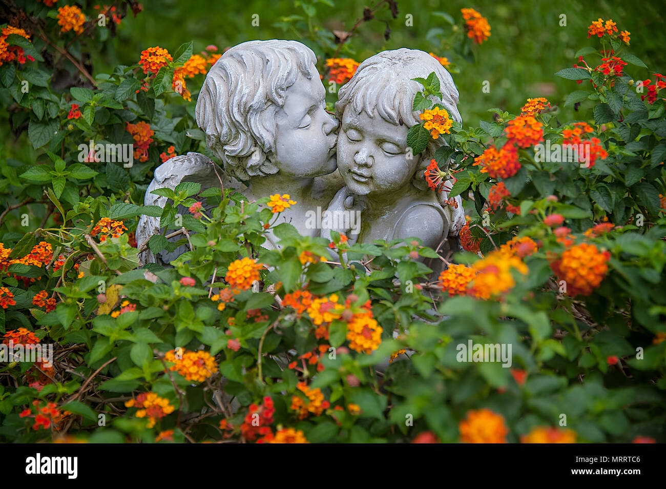 Engel in der Liebe. Skulpturen von Jungen und Mädchen Engel mit Blumen umarmen und knuddeln umgeben. Der junge Engel ist sie zu küssen von der Wange. Stockfoto