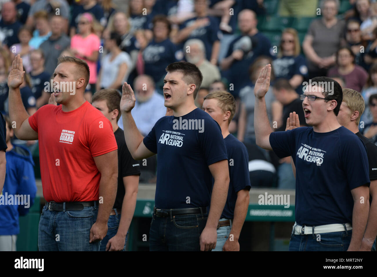 North Dakota Air National Guard Rekruten Riley Wilhelm, rechts, und Peter Griffin, Mitte, sind unter enlistees Anheben der rechten Hand, als sie das US-Militär Eid der Dienstzeit während einer Zeremonie im militärischen Anerkennung Nacht im FM RedHawks Baseballspiel schwören, Newman, Fargo, N.D., 29. Juni 2017. (U.S. Air National Guard Foto von Senior Master Sgt. David H. Lipp/Freigegeben) Stockfoto
