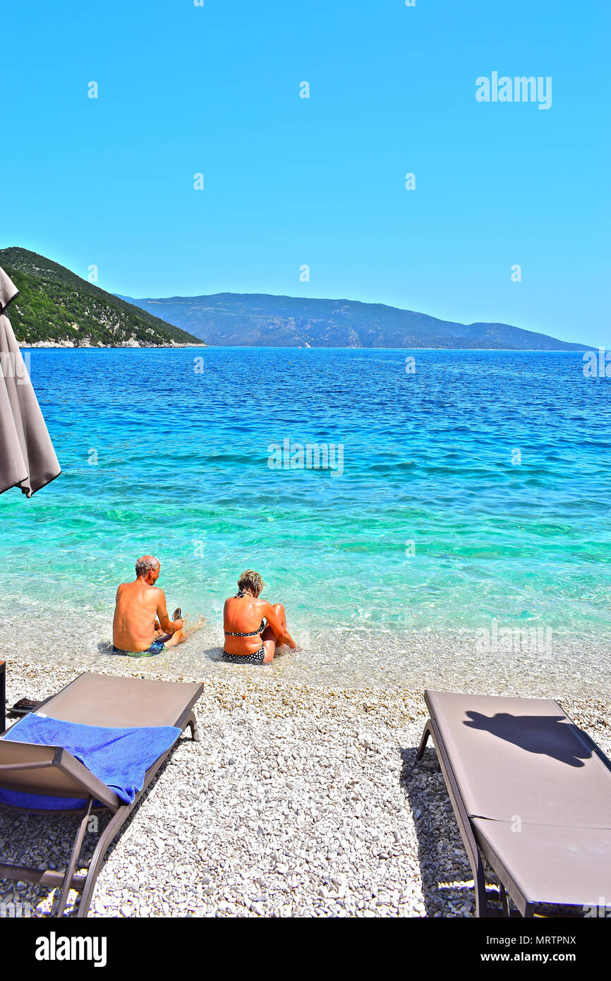 Ein älteres Paar Spaß und genießen Sie im kristallklaren Wasser des Ionischen Meeres an Antisamos Beach in der Nähe von Sami, Kefalonia, Griechenland sitzen. Stockfoto