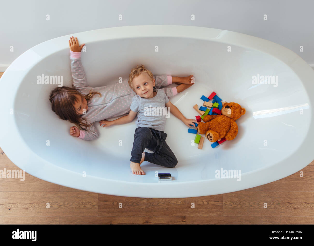 Ansicht von oben Kinder liegen in der Badewanne mit Teddybär und Holzklötze. Kleinen Geschwister in einer Badewanne zu spielen. Stockfoto