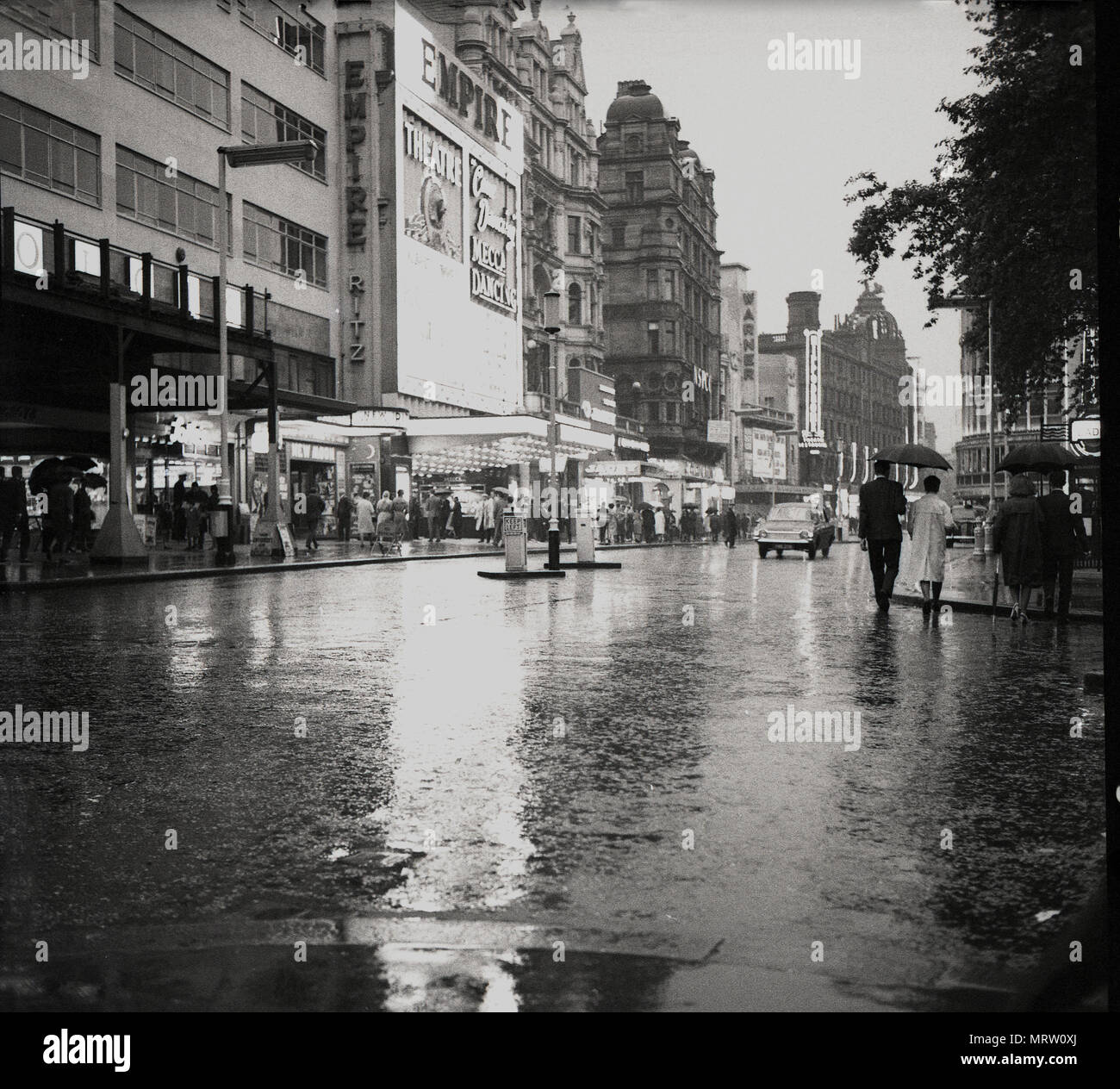 1960, historische Ansicht eines nassen, feuchten, ziemlich spärlich Leicester Square, London, England, zeigt das Empire Theater, ursprünglich im Jahr 1884 für verschiedene Theater gebaut und dann wieder in den 1920er Jahren für das Zeigen von Spielfilmen. In Mecca Bingo 1961 übernahm das Imperium und verwandelte es in einem MGM Kino und ein Mekka Dance Hall. In dieser ära Verkehr könnte gehen hinter dem Empire, etwas, das nicht geschehen. Stockfoto
