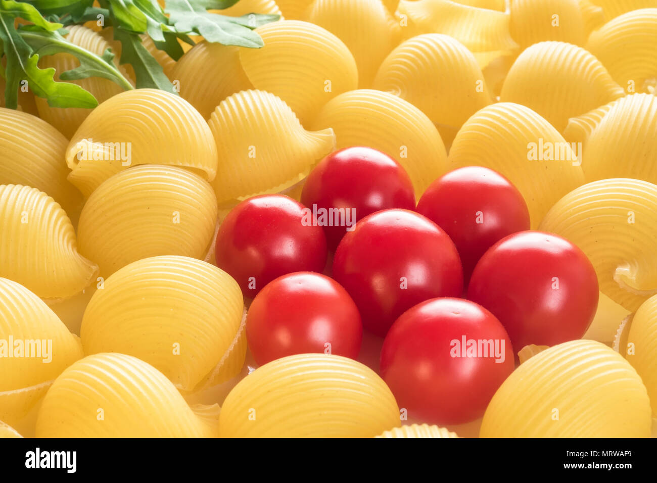 Essen Hintergrund ungekochtes Macaroni Lumaconi Nahaufnahme makro Red Cherry Tomaten in Blütenform und Blätter Rucola Salat Zutaten für Pa-set Stockfoto