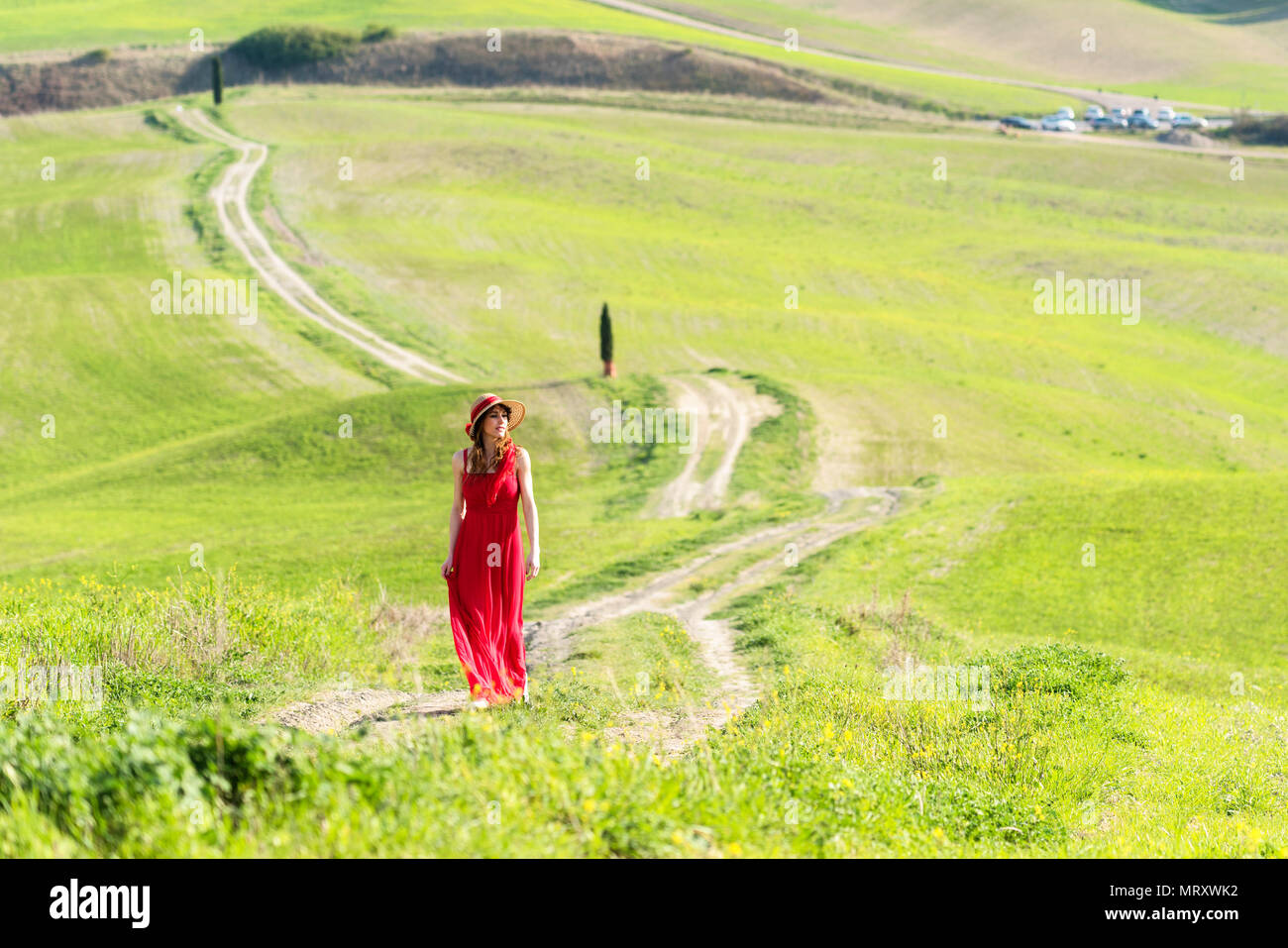 San Quirico d'Orcia, Val d'Orcia, Siena, Toskana, Italien. Eine junge Frau im roten Kleid auf einem Feldweg in der Nähe der Zypressen von Val d'Orcia Stockfoto