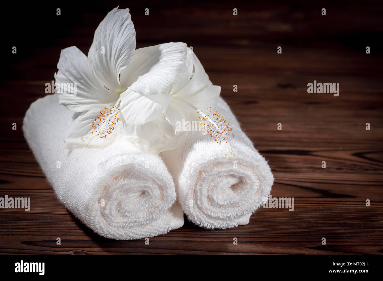 Spa Konzept der weiche, weiße Handtücher aus Baumwolle gerollt und Blüten von Hibiskus auf Holz Textur, in der Nähe Stockfoto