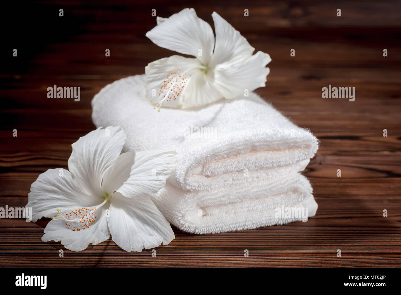 Spa Konzept der weiche, weiße Handtücher aus Baumwolle gefaltet und Blüten von Hibiskus auf Holz Textur, in der Nähe Stockfoto