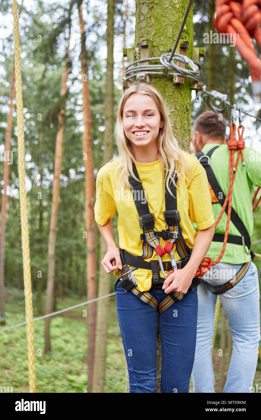 Glückliche junge Frau, die als Anfänger beim Klettern im Hochseilgarten mit Kabelbaum Stockfoto