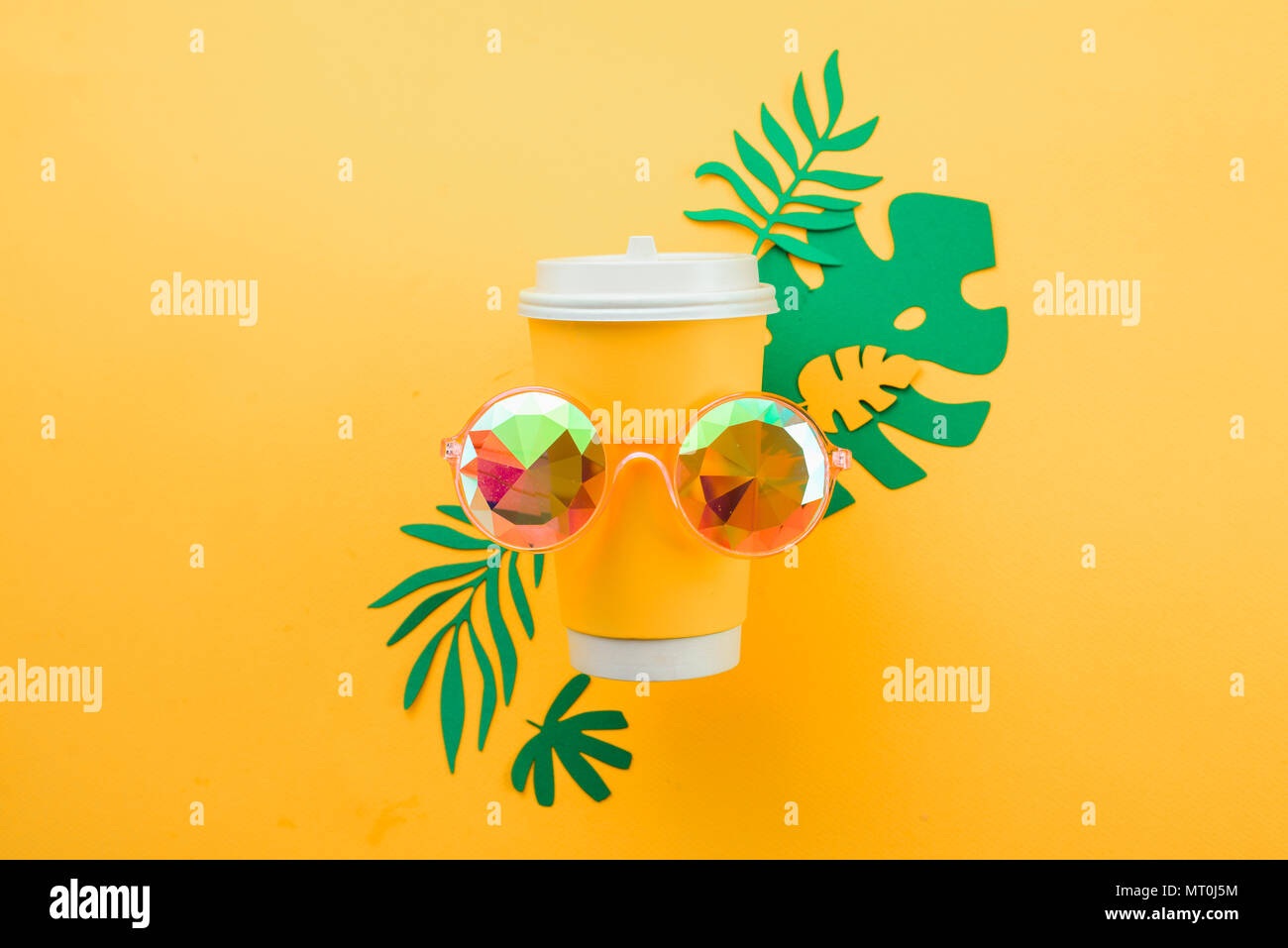 Frische Sommer drink-Konzept. Das verfügbare Papier Schale in Sonnenbrille auf gelbem Hintergrund mit tropischen Blättern Stockfoto