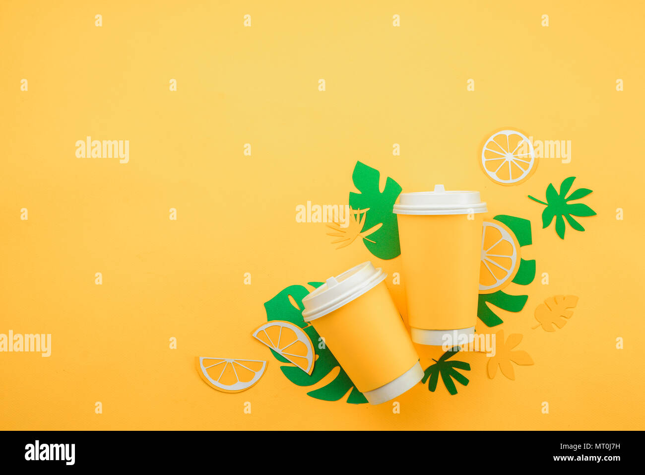 Farbenfrohe Sommer trinken Konzept. Verfügbare Pappbecher auf gelbem Hintergrund mit tropischen Blättern und Orangenscheiben auf einem gelben Hintergrund. Stockfoto