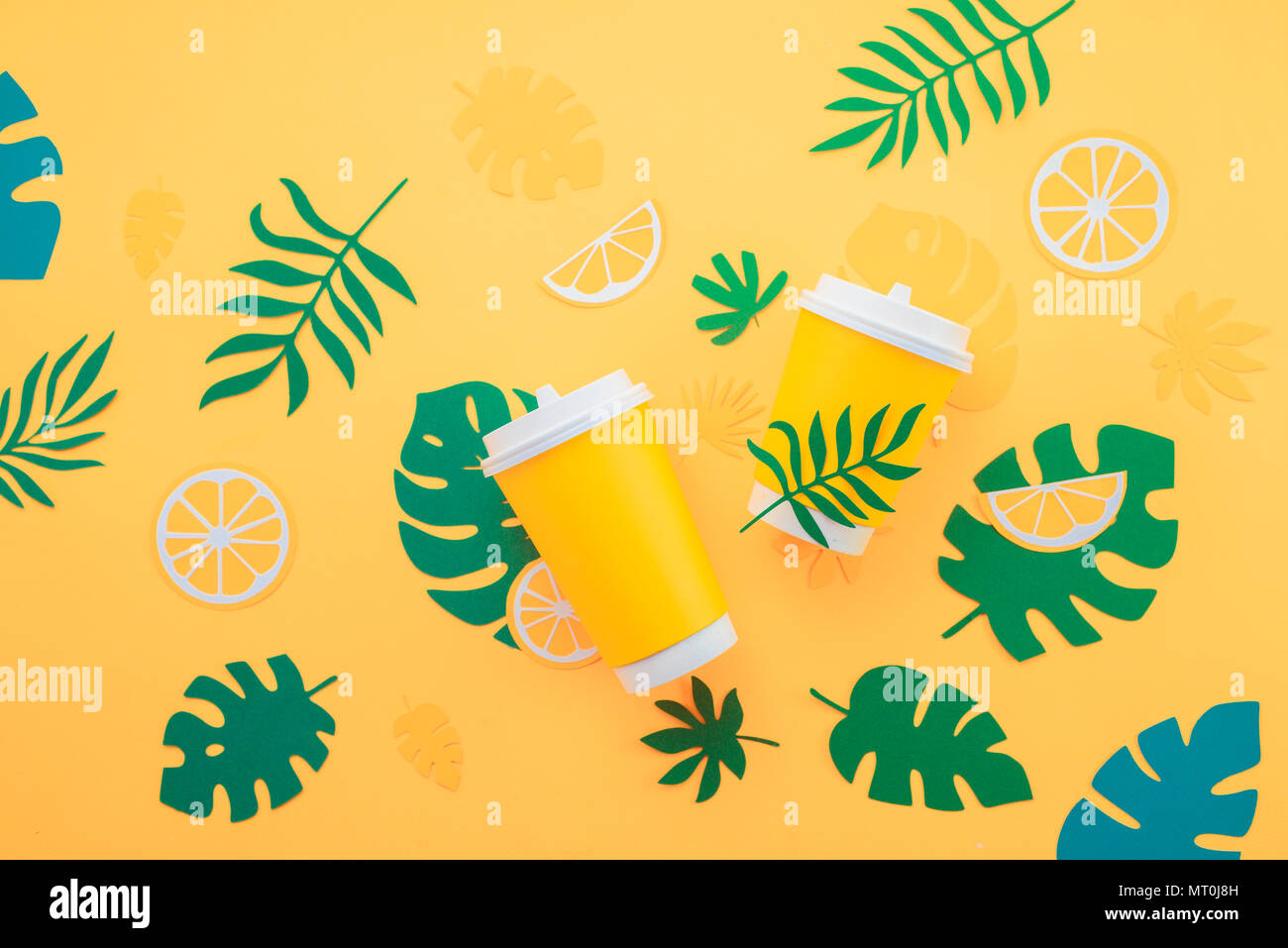 Verfügbare Pappbecher auf gelbem Hintergrund mit tropischen Blättern und Orangenscheiben auf einem gelben Hintergrund. Farbenfrohe Sommer trinken Konzept mit p Stockfoto