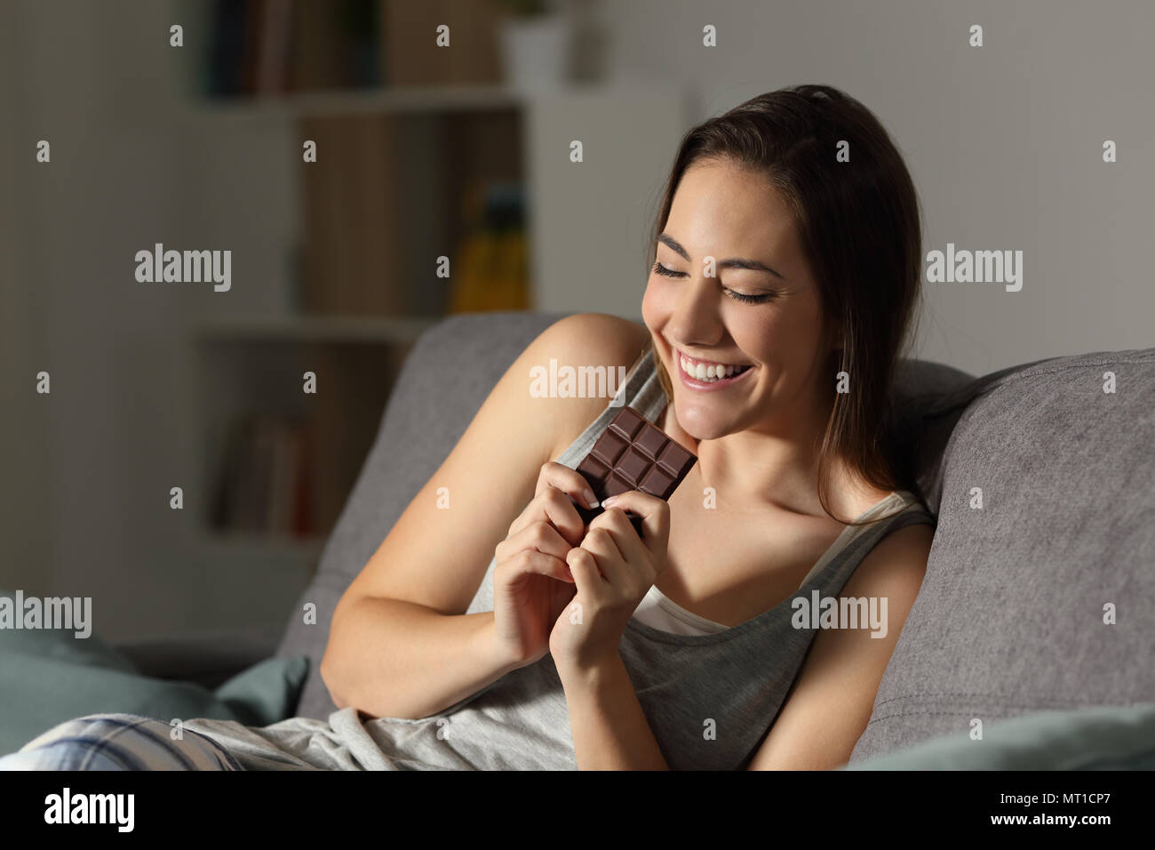 Glückliche Frau Schokolade essen in der Nacht auf einer Couch im Wohnzimmer zu Hause sitzen Stockfoto