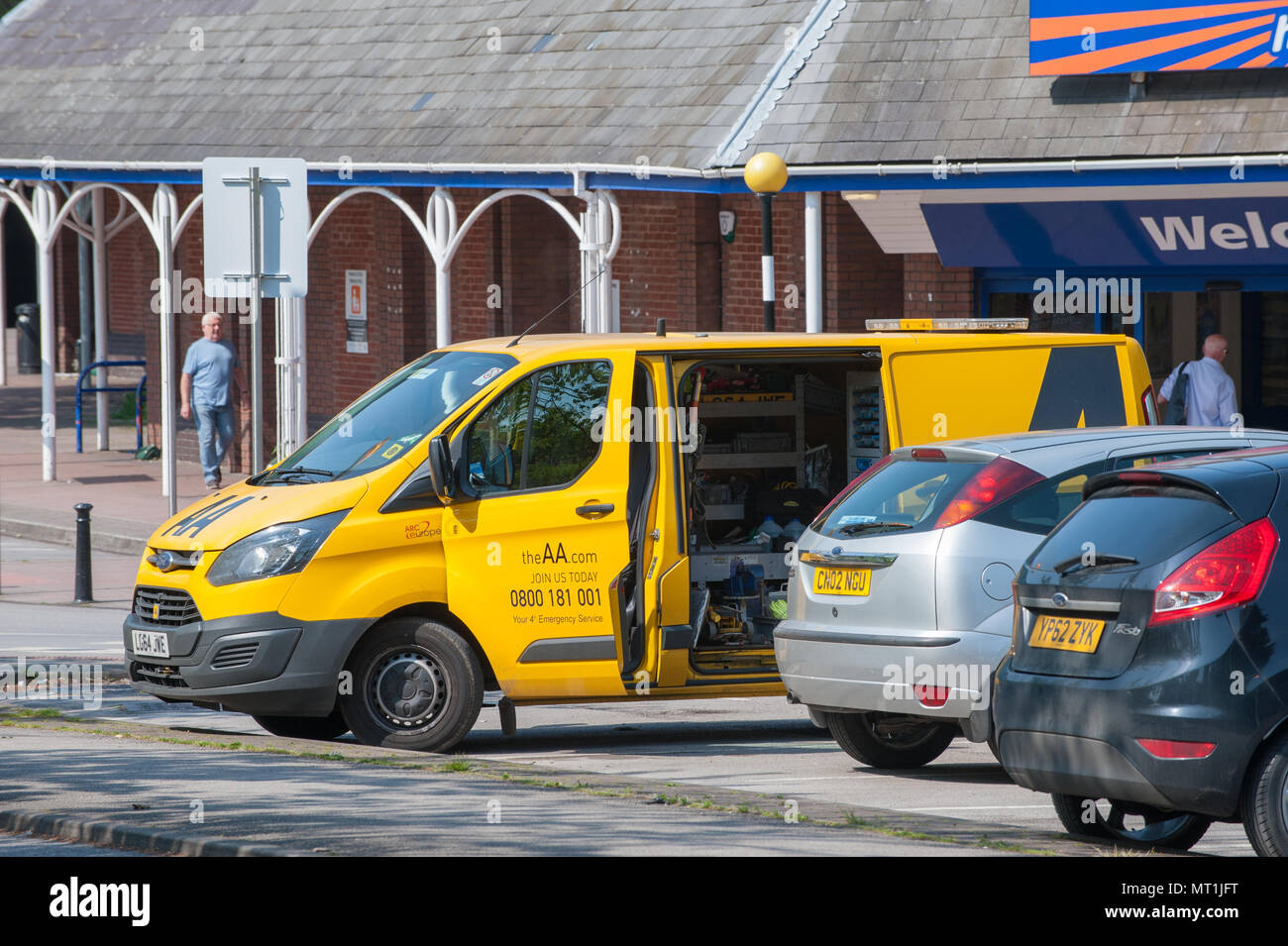 AA-Lieferwagen für Pannenhilfe, der vor einem Supermarkt in Doncaster, Großbritannien, geparkt ist, mit offener Seitentür, während ein Mechaniker auf einem belebten Parkplatz ein Fahrzeug betreut Stockfoto