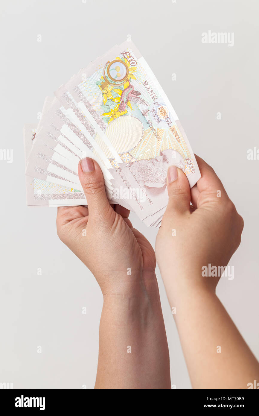 Zehn Pfund Noten der Bank von England in weibliche Hände. Close-up Fotos über grauer Hintergrund mit selektiven Fokus Stockfoto