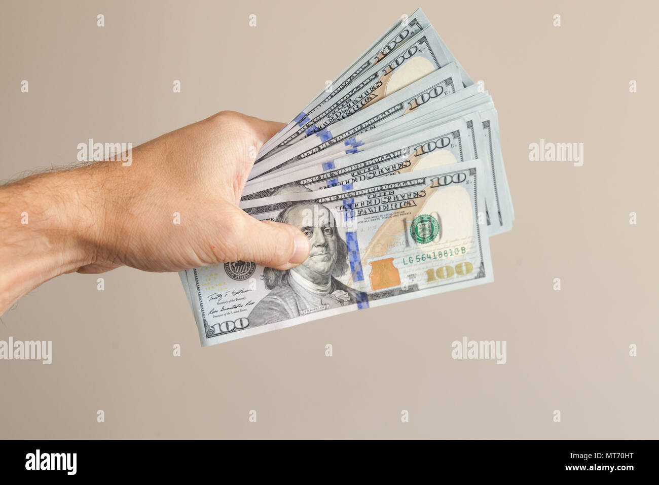 100 Dollar Noten in männlicher Hand über grauer Hintergrund Stockfoto