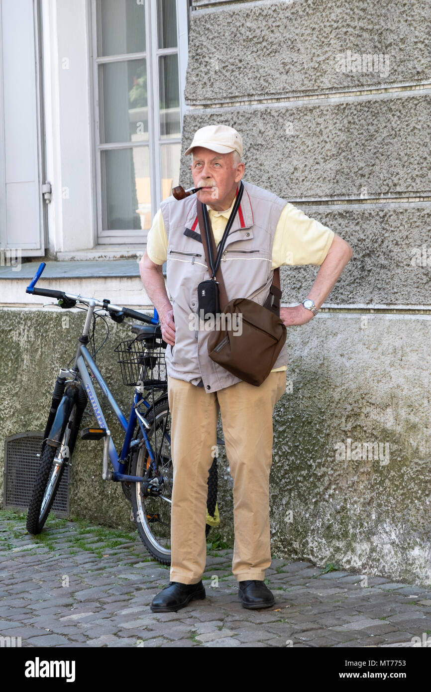 Ein Tourist mit einer Kamera und mann Beutel Rauchen eine Rohrleitung auf einer Nebenstraße in Regensburg, Deutschland Stockfoto