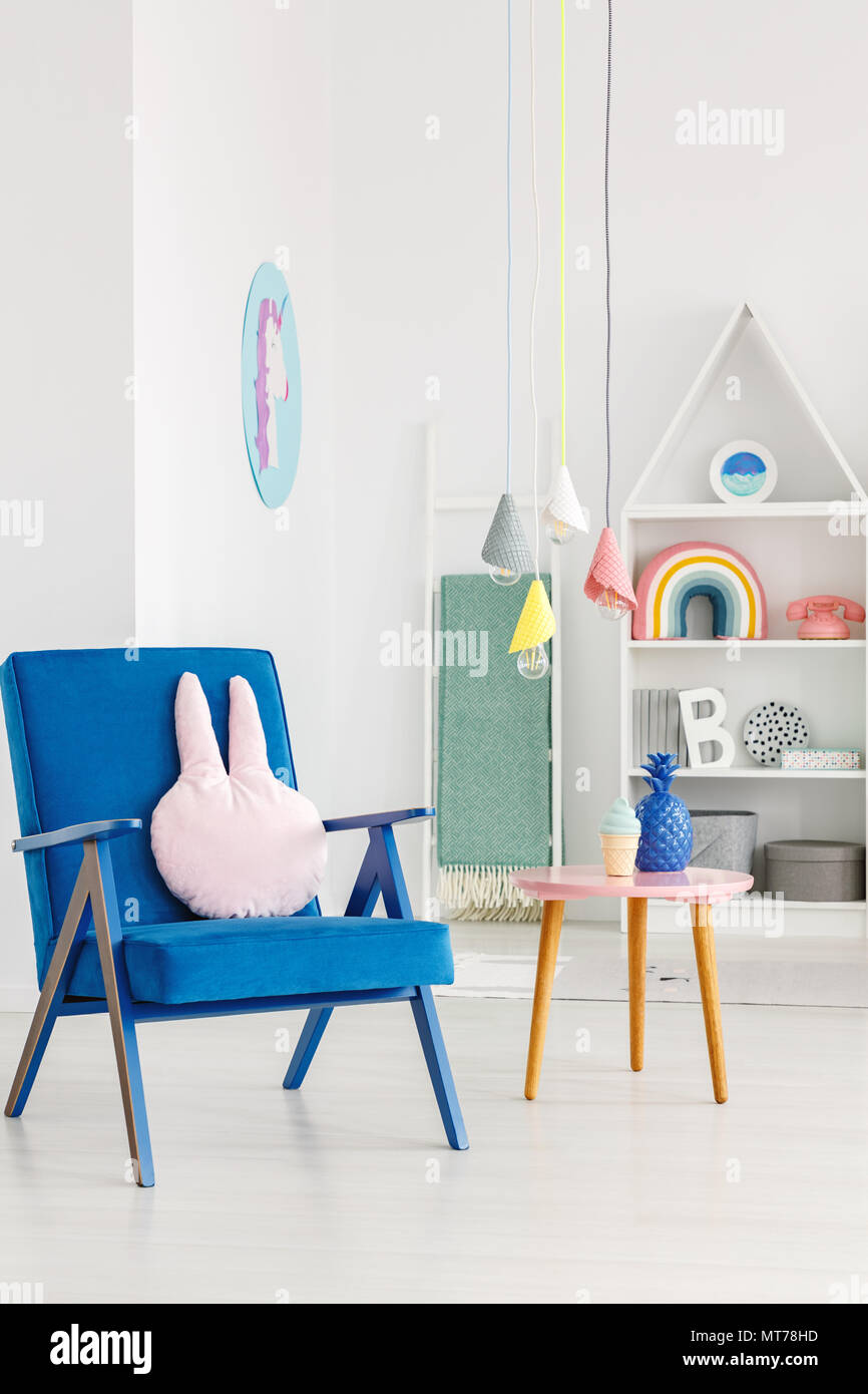 Marine Blau Sessel mit einem Kaninchen Kissen neben einem Tisch und weiße Regale im Hintergrund in ein Kinderzimmer Innenraum Stockfoto