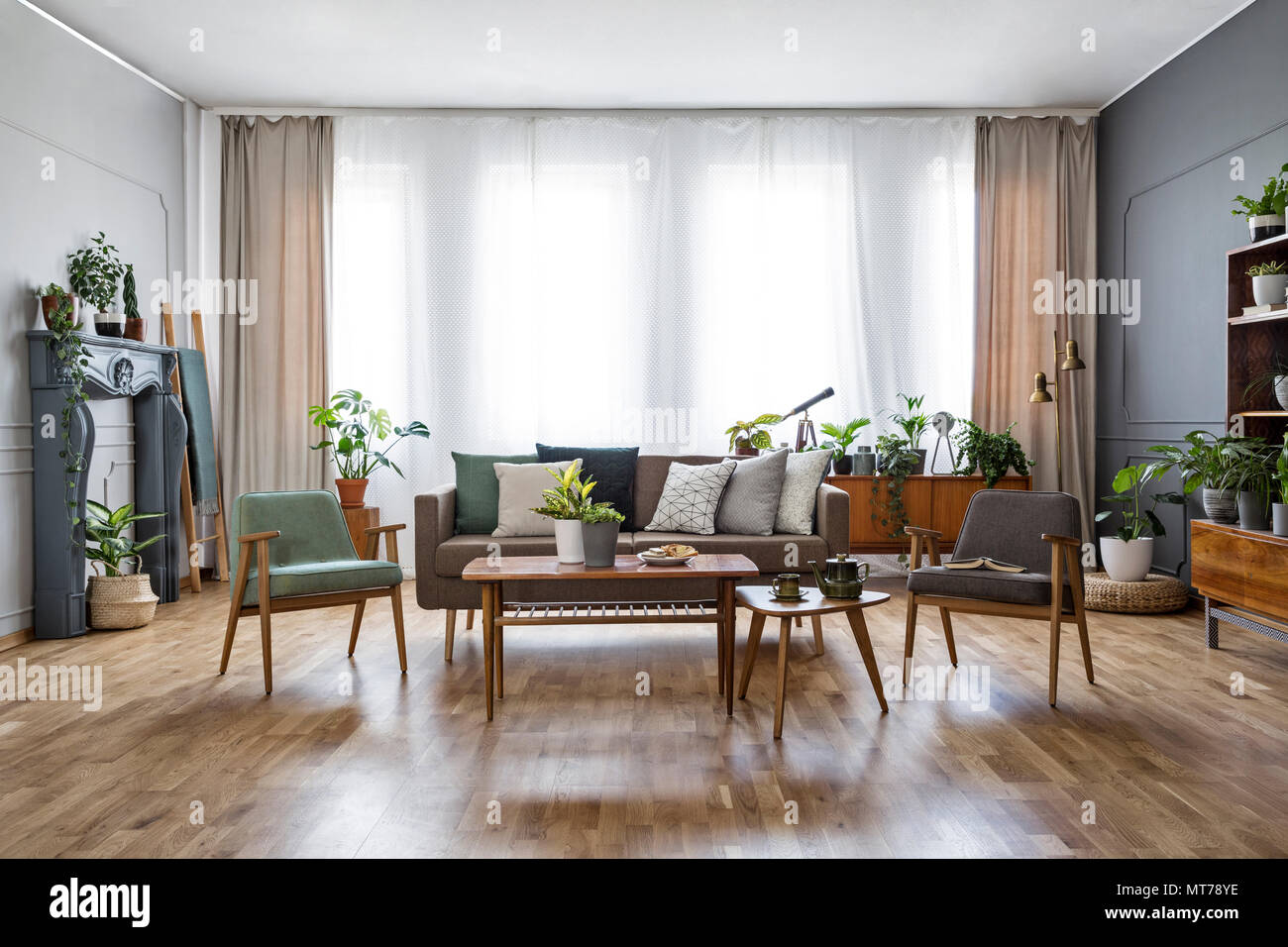 Holztisch mit Blumen zwischen Sessel im geräumigen Wohnzimmer mit Sofa. Real Photo Stockfoto