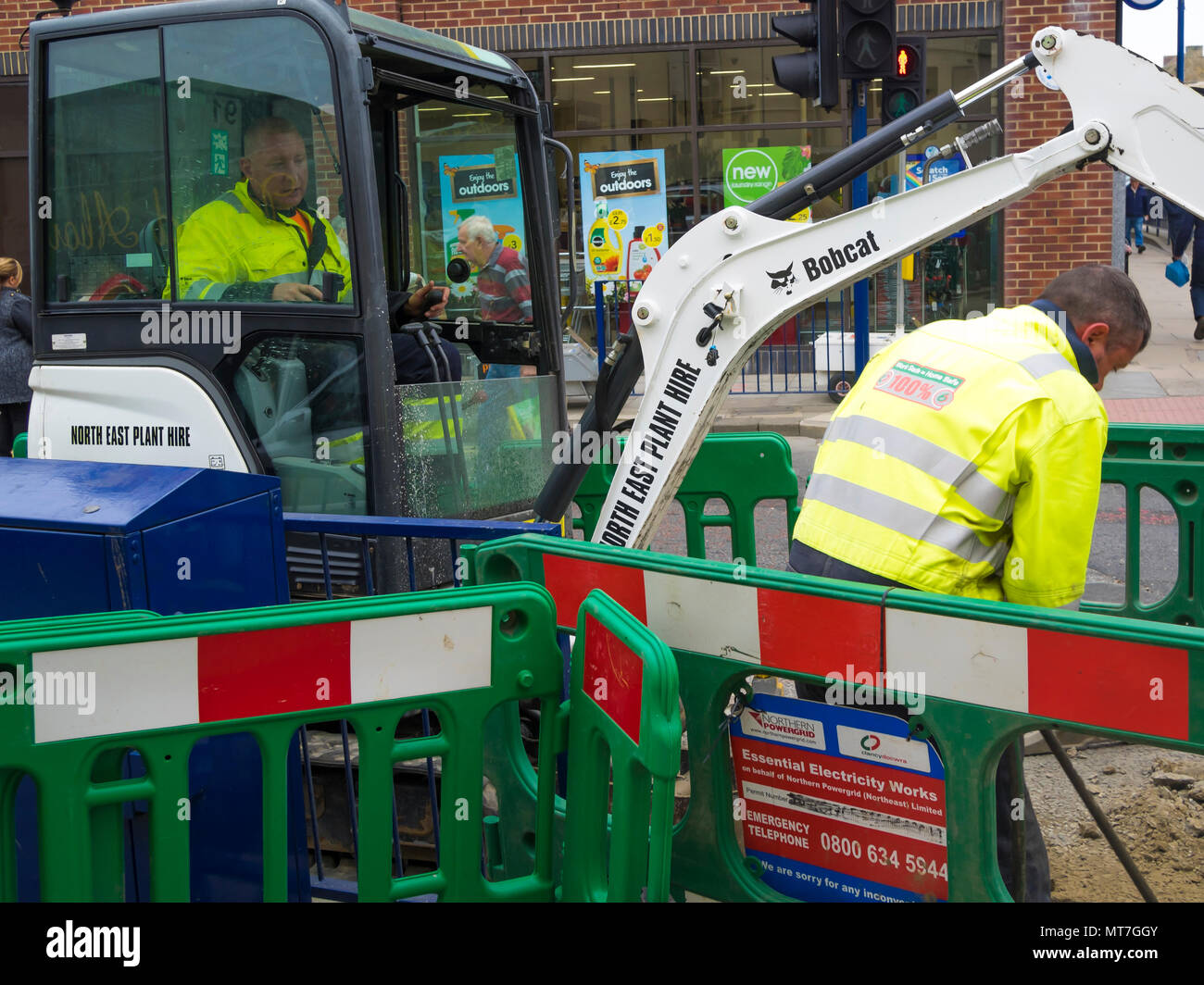 Handwerker Betrieb eines kleinen Bobcat Bagger Graben in der Fahrbahndecke, die für die Installation eines elektrischen Kabel Stockfoto