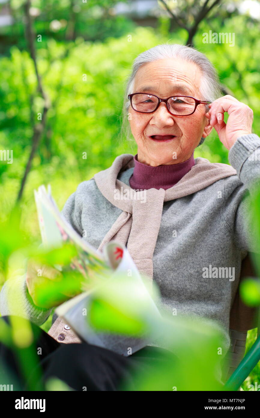 Eine glückliche hochrangigen chinesischen Frau liest Buch im Hof Stockfoto