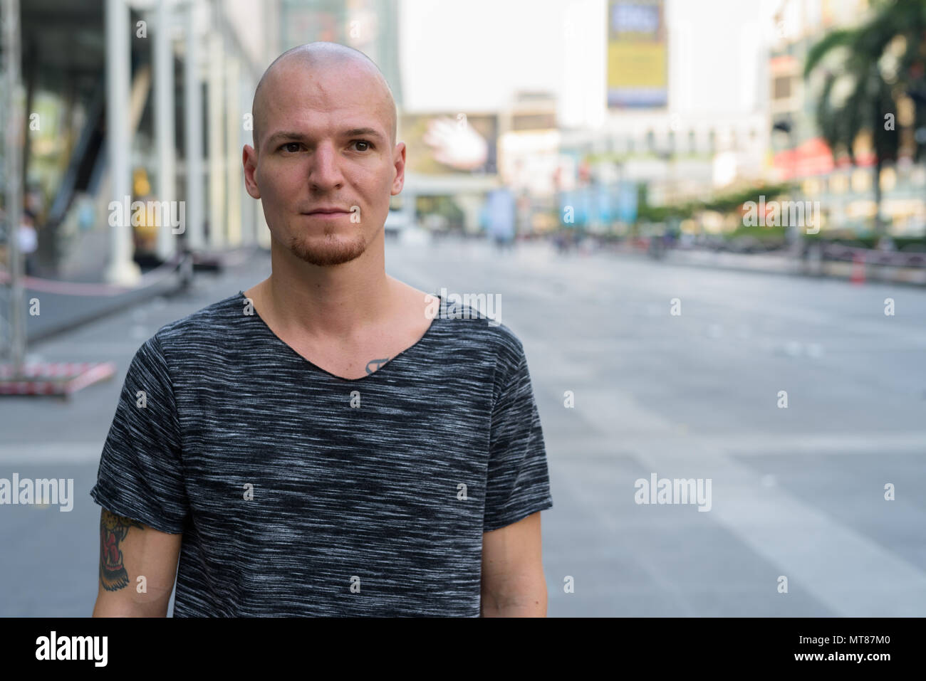 Junge schöne glatzköpfige Mann Denken außerhalb der Mall in Bangkok. Stockfoto