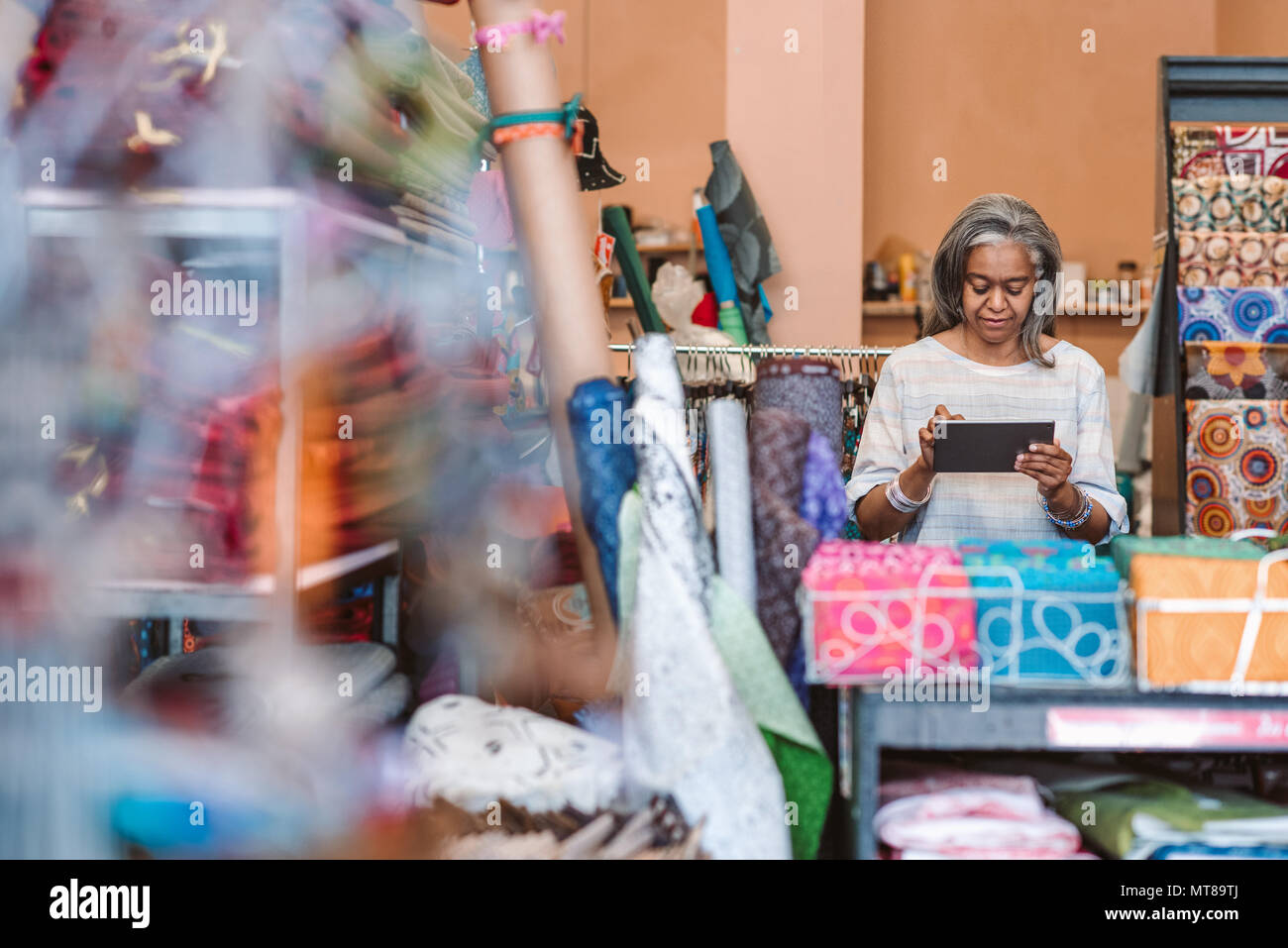 Reifen Stoff shop besitzer arbeiten mit einem digitalen tablet, während bei einem Zähler von bunten Tüchern und Textilien umgeben stehend Stockfoto