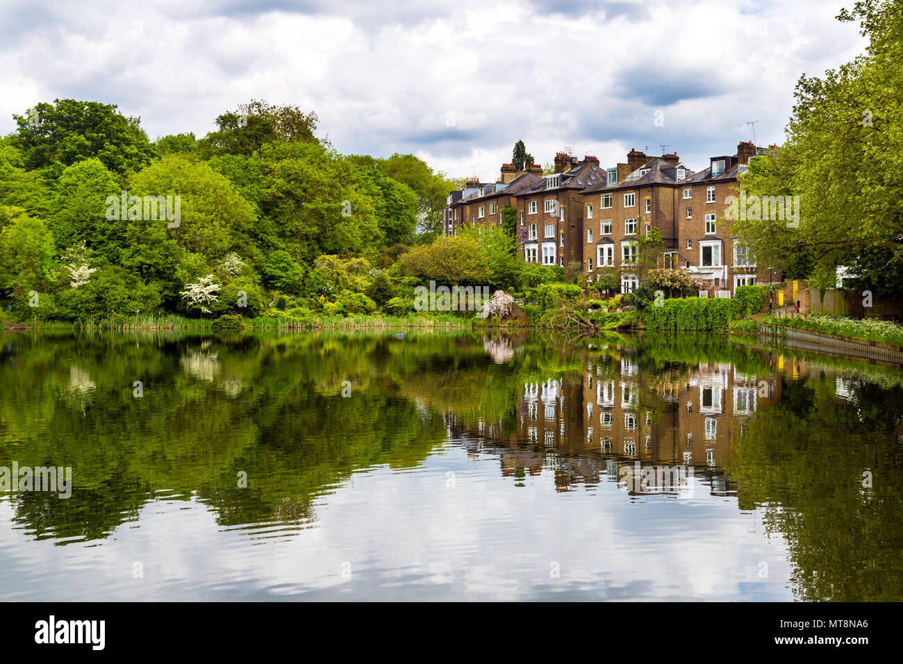 Häuser von South Hill Park, mit Blick auf einen See mit einer lebendigen Reflexion an Hampstead Heath, London, UK Stockfoto