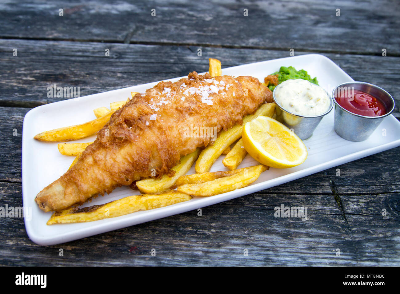 Platte von Panierten Fisch und Chips mit Erbsenpüree und Sauce Tartar, serviert auf einem Holztisch Stockfoto