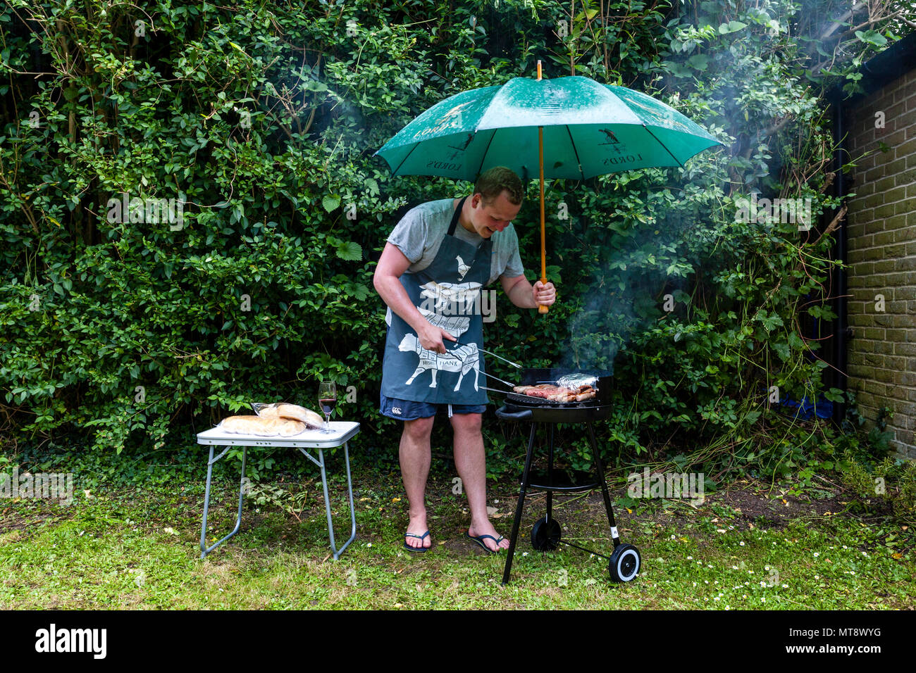 Lewes, Sussex, UK. 28. Mai 2018. Ein junger Mann kocht das Essen auf einem Grill während einer Regendusche. Credit: Grant Rooney/Alamy leben Nachrichten Stockfoto