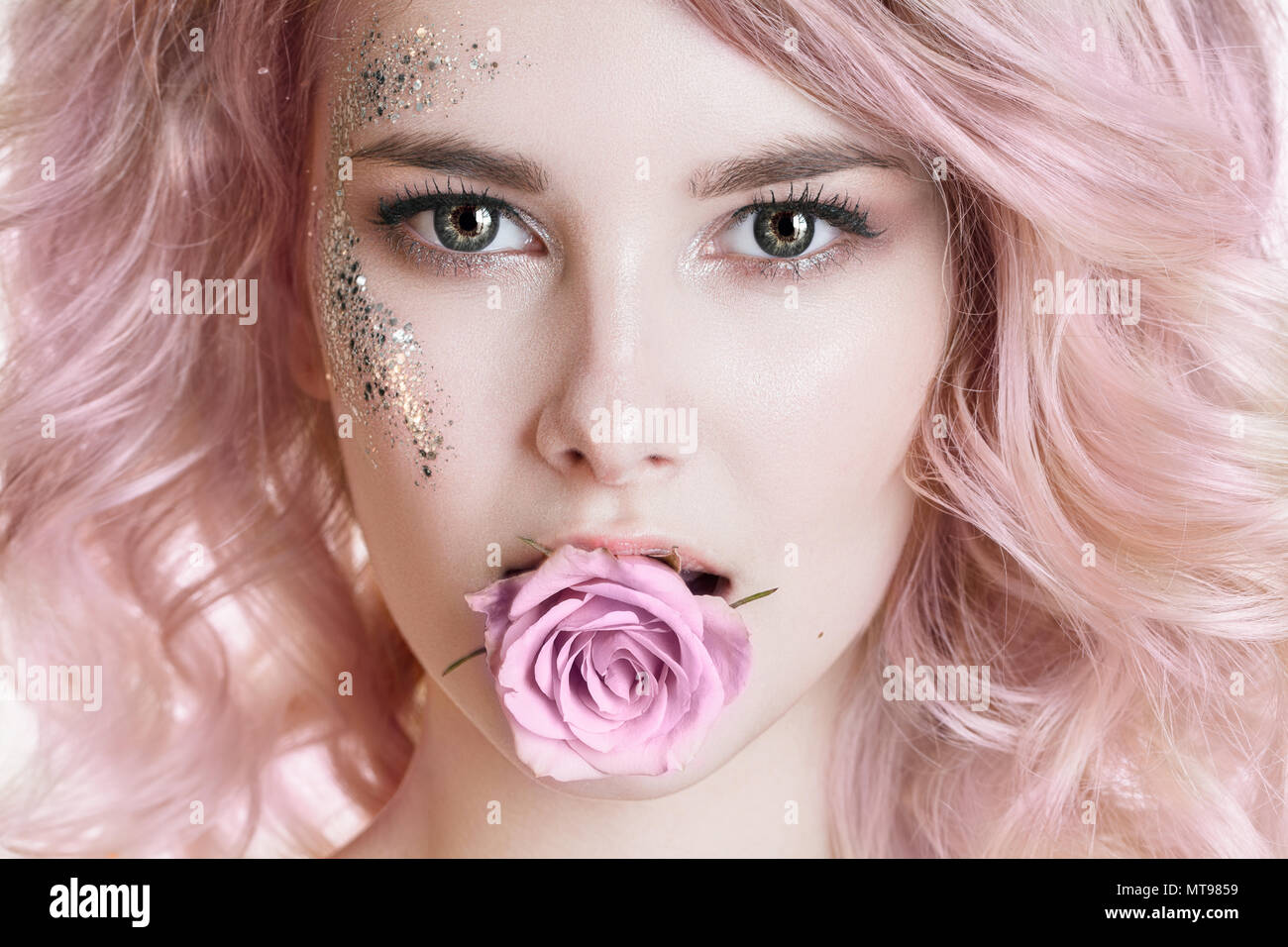 Gefärbte Haare. Schönheit Frauen Porträt der jungen Frau mit rosa lockiges Haar, perfekte Kunst Make-up mit Glitzer. Rose im Mund Stockfoto