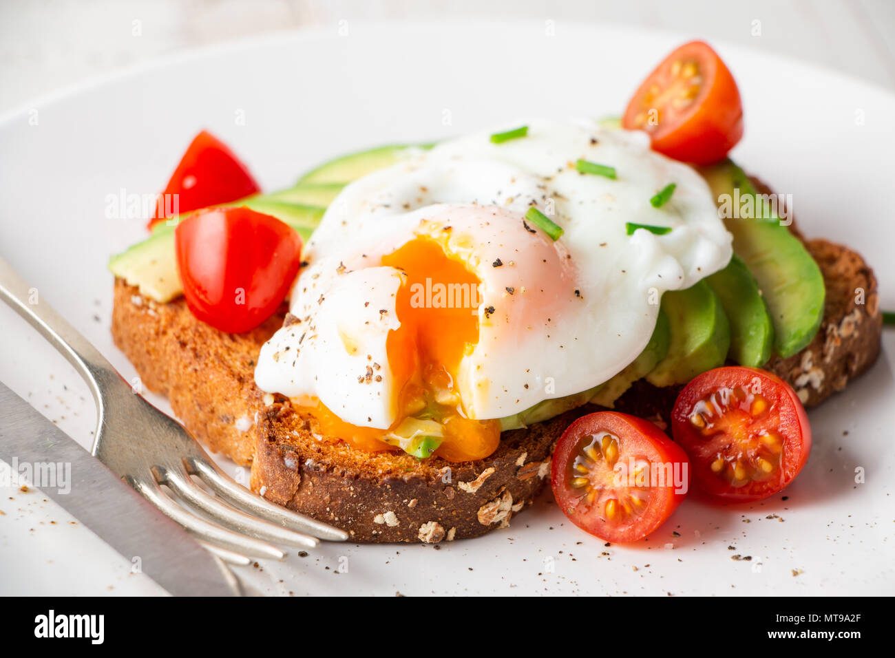 Gesundes Vollkornbrot Toast mit Avocado, pochiertes Ei, Cherry Tomaten und Baby Blätter Salat Stockfoto