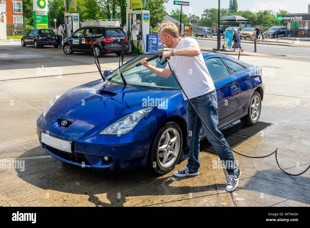 Männlich (Alter 30-40 Jahre) über eine Düse Hochdruckreiniger waschen einen blauen Toyata Celica Auto an einer Tankstelle in Großbritannien, Europa zu reinigen Stockfoto