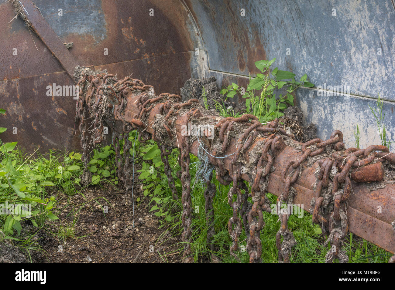 Blick in die Trommel eines Dreschkolbenstreuers mit Drehschlegelketten, dessen Unkraut in altem Dreck wächst - typische Landmaschinen und rostige Ketten. Stockfoto