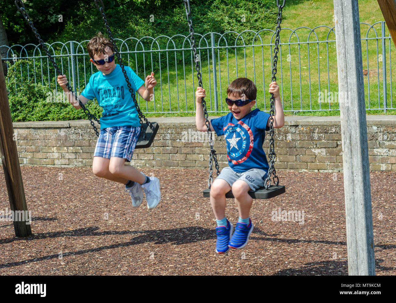 Junge Brüder spielen auf Schaukeln auf dem Spielplatz in der Junggesellen Morgen in Windsor, UK. Stockfoto