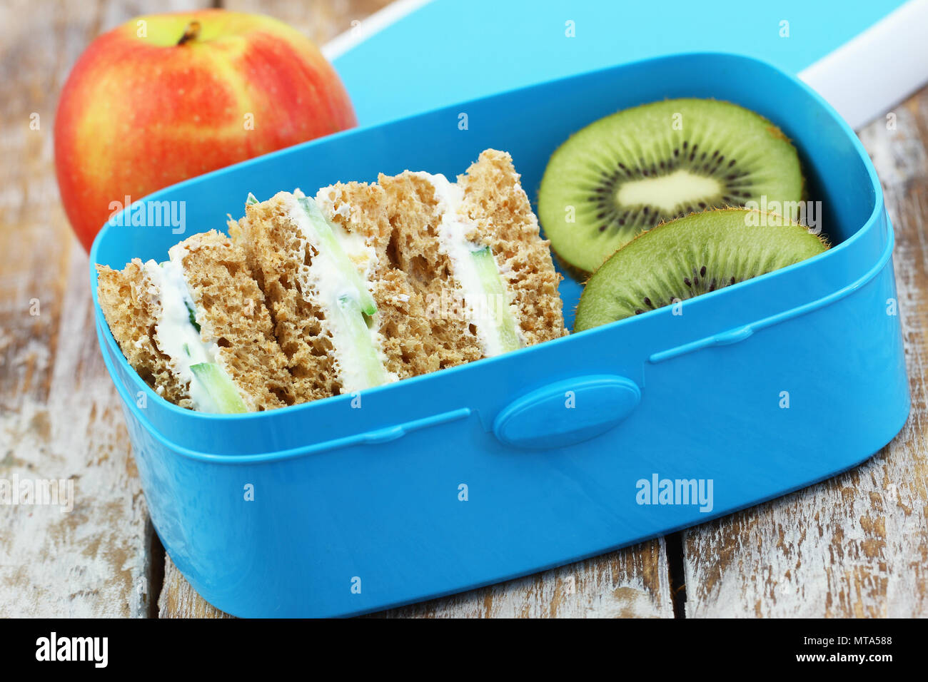 Braun creme Käse und Gurke Sandwiches in Lunch Box, Kiwi und Apple Stockfoto
