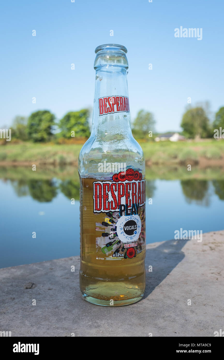 Nahaufnahme einer halb leeren Flasche Desperados Bier, die an einem sonnigen Morgen im Sommer am Fluss Nith, Kingholm Quay, Schottland, verlassen wurde. Stockfoto