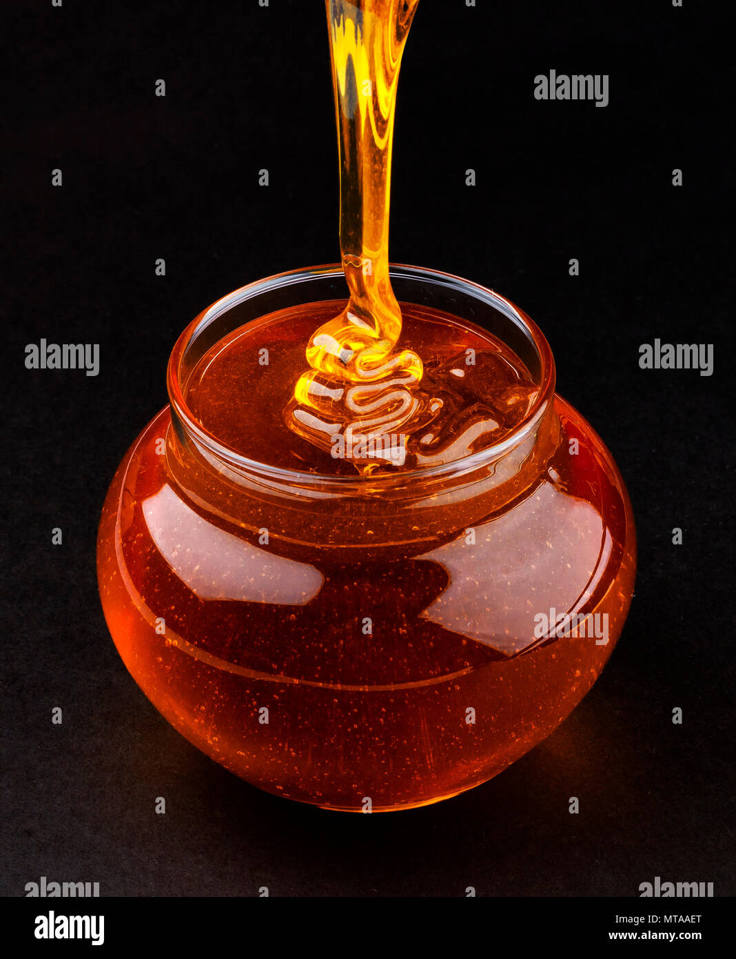 Topf gießen Honig auf schwarzem Hintergrund Stockfoto