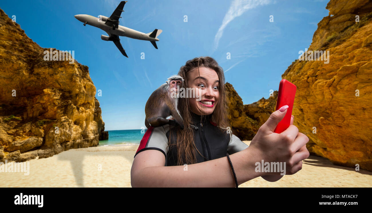 Nette weibliche sportman Windsurfer in Neoprenanzug mit Telefon am Strand, Affe sitzt auf ihre Schulter, Flugzeug fliegen auf Hintergrund Stockfoto