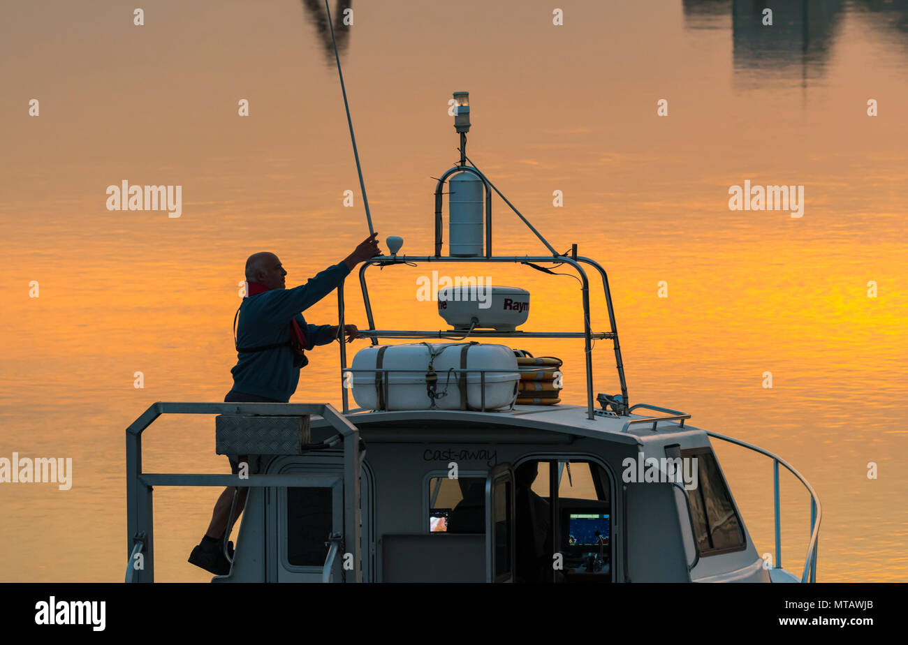 Boot auf einem Fluss in der Dämmerung, nach Hause kommen nach einer Reise auf dem Meer, mit Abendlicht und orange Reflexionen der Abendhimmel in Wasser. Going home Konzept. Stockfoto