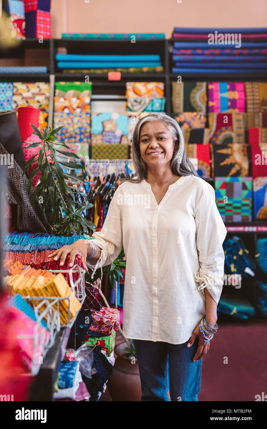 Porträt eines lächelnden reife Stoff shop besitzer stehen in ihrem Store von Racks und Regale voll von bunten Tüchern und Textilien Stockfoto