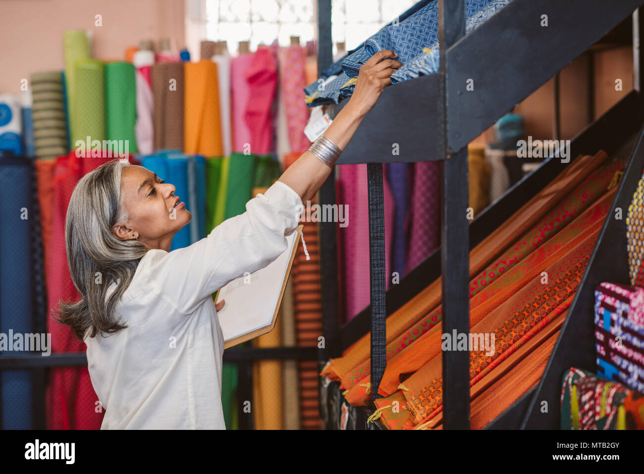 Reifen Stoff shop besitzer arbeitet sie in ihrem Store von bunten Tüchern und Textilien Bestandsaufnahme mit einem Klemmbrett umgeben Stockfoto