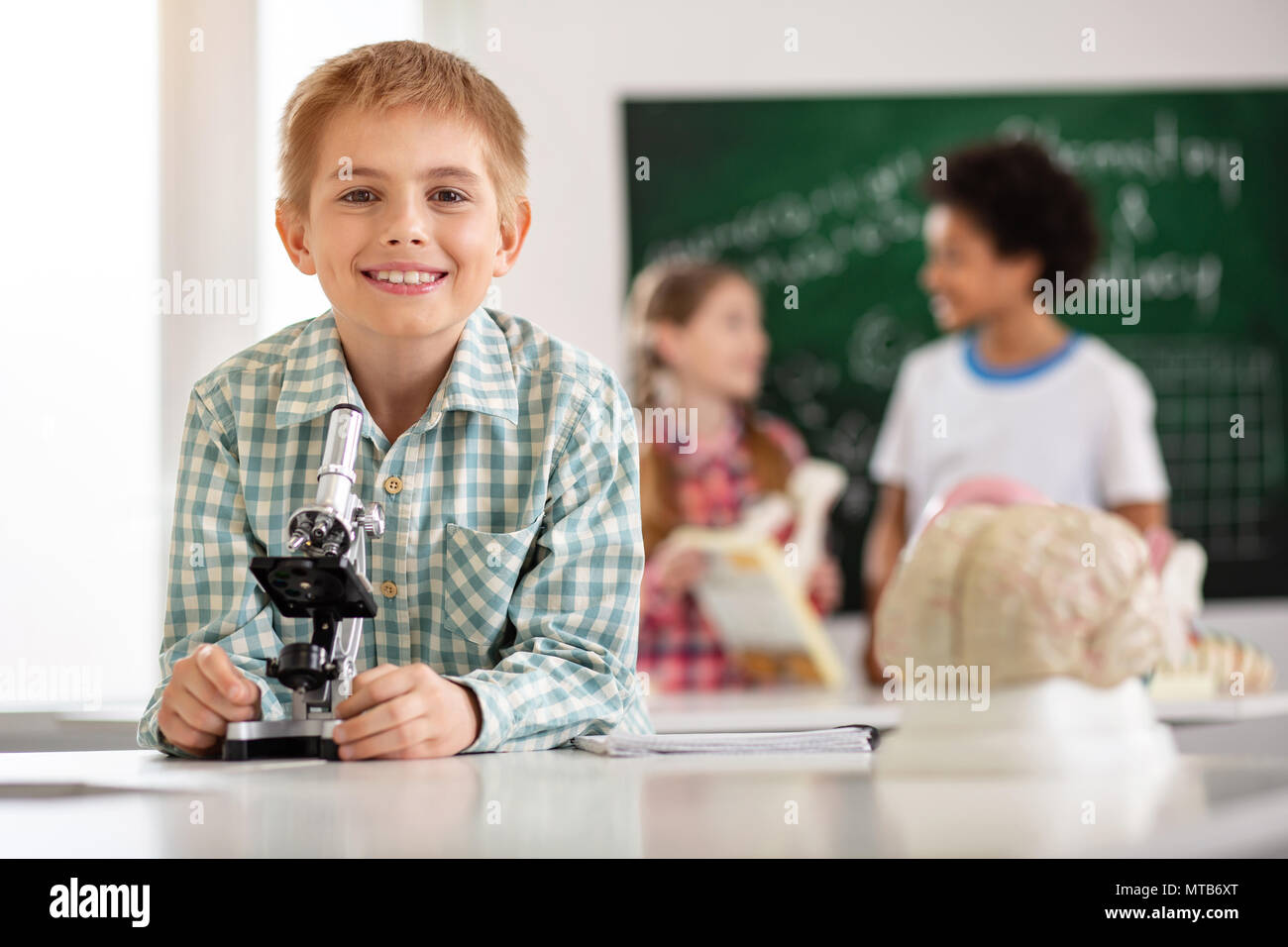 Fröhliche glückliche Schüler stehen vor dem Mikroskop Stockfoto