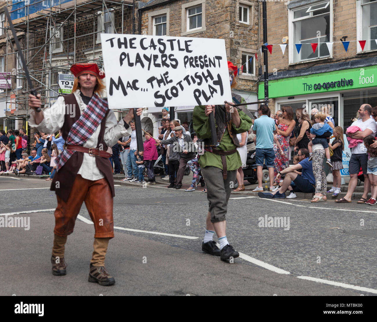Die Parade durch die Main Street am Barnard Castle, England, Großbritannien mit zwei Männern angezogen und mit einem Banner, das Schloss Spieler Förderung Stockfoto