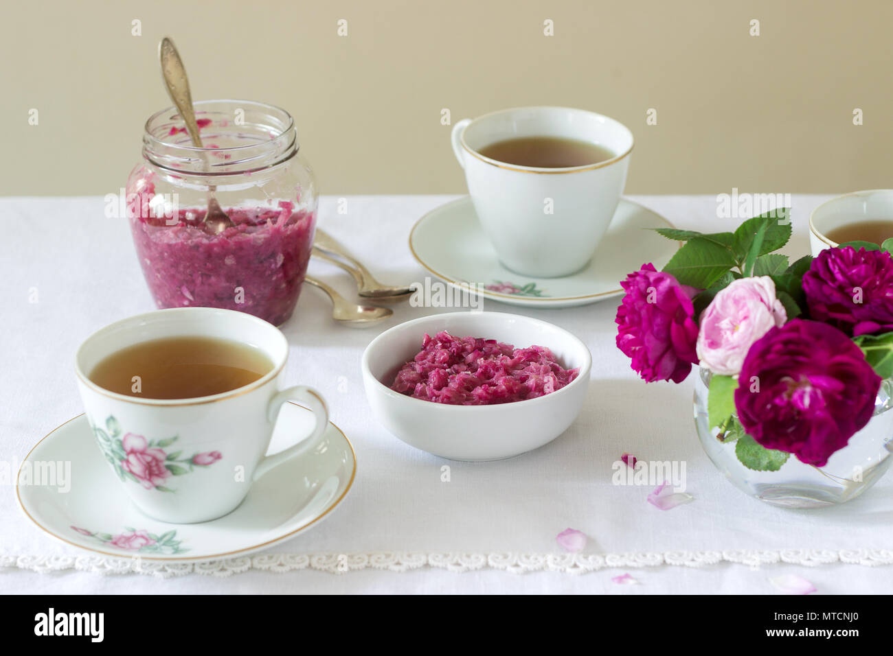 Stau in die Blütenblätter der Damaskus Rose, eine Tasse grünen Tee und eine Vase mit Rosen auf einem Leuchttisch. Rustikaler Stil, selektiven Fokus. Stockfoto
