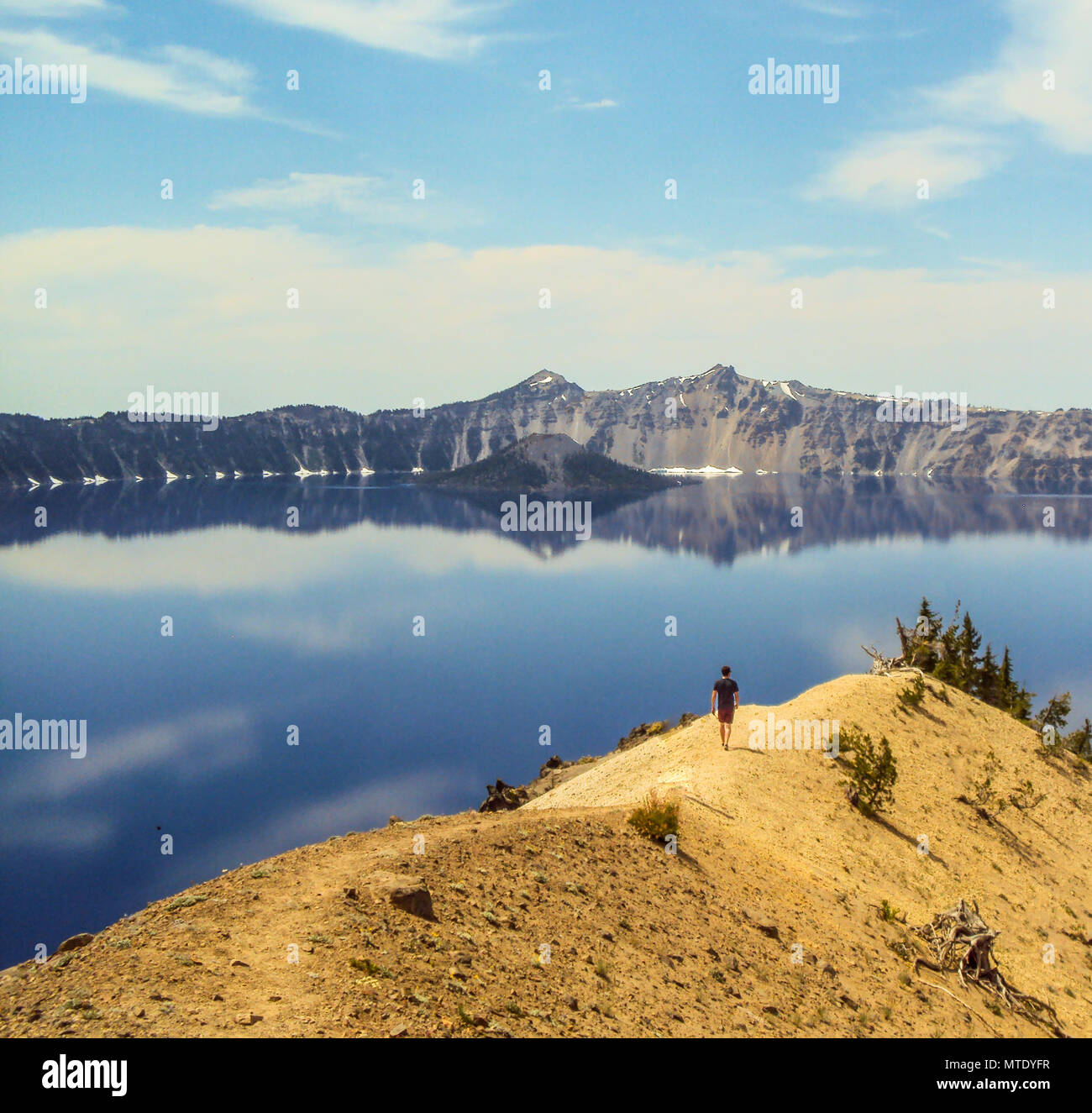 Mann zu Fuß entlang dem Kamm eines Berges Richtung Wasser der Crater Lake, Oregon Stockfoto